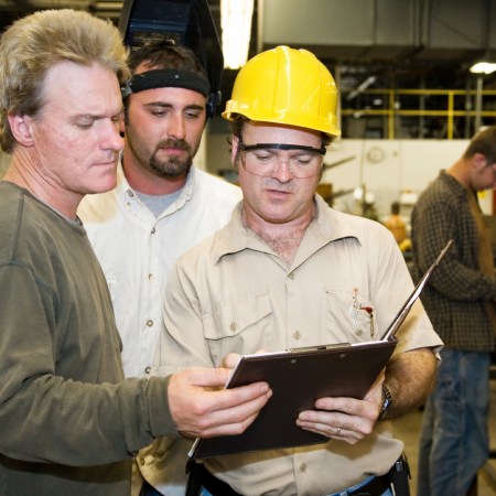 Factory worker and foreman discuss inspection report with auditor.