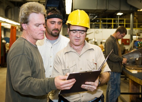 Factory worker and foreman discuss inspection report with auditor.